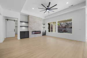 Unfurnished living room with light hardwood / wood-style floors, a barn door, a fireplace, and ceiling fan