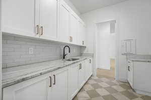 Kitchen featuring decorative backsplash, white cabinets, sink, and light stone counters