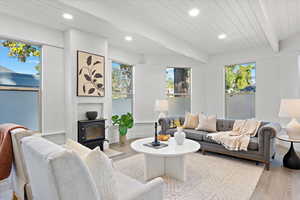 Living room featuring a wood stove, beam ceiling, wood ceiling, and light wood-type flooring