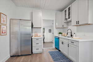 Kitchen with sink, appliances with stainless steel finishes, light wood-type flooring, and white cabinets