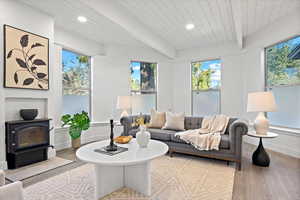 Living room with light hardwood / wood-style floors, a wood stove, beam ceiling, and wooden ceiling