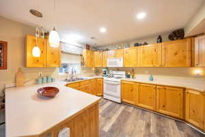 Kitchen with sink, kitchen peninsula, dark hardwood / wood-style floors, decorative light fixtures, and white appliances