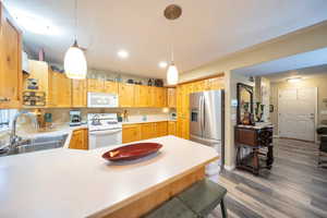 Kitchen with sink, kitchen peninsula, hanging light fixtures, white appliances, and dark hardwood / wood-style flooring