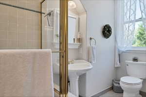 Bathroom off spare bedrooms with toilet, tile patterned floors, and a shower with door