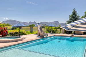 View of pool featuring a patio area, a water slide, a mountain view, and an in ground hot tub