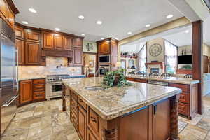 Kitchen featuring light stone countertops, Wolf and Subzero appliances, decorative backsplash, and a center island with sink