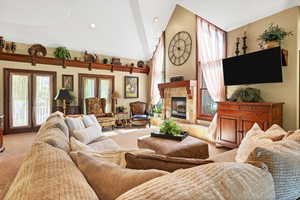 Living room off kitchen featuring French doors, light carpet, a healthy amount of sunlight, and a fireplace