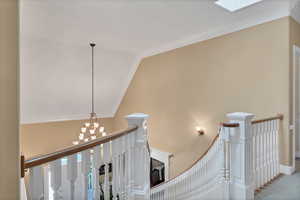 Staircase to level 2 and basement, lofted ceiling with skylight, ornamental molding, and a chandelier