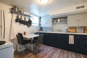 Kitchen with stainless steel fridge, dark wood-type flooring, white cabinetry, and backsplash