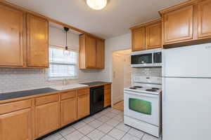 Kitchen featuring decorative backsplash, hanging light fixtures, sink, light tile patterned floors, and white appliances