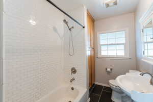 Full bathroom featuring a wealth of natural light, sink, tiled shower / bath, and toilet