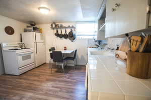 Kitchen with dark hardwood / wood-style flooring, a textured ceiling, ornamental molding, sink, and white appliances