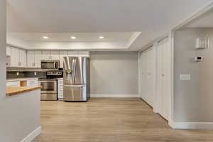 Kitchen featuring appliances with stainless steel finishes, light hardwood / wood-style flooring, white cabinetry, and backsplash