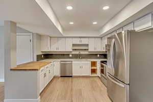 Kitchen featuring appliances with stainless steel finishes, sink, wood counters, white cabinets, and light hardwood / wood-style flooring