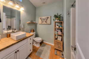 Bathroom with a textured ceiling, walk in shower, wood-type flooring, toilet, and vanity with bamboo countertops