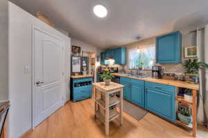 Kitchen with sink, light wood-type flooring, blue cabinets, and hanging light fixtures