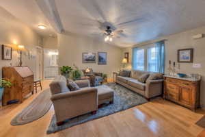 Living room with vaulted ceiling, a textured ceiling, light hardwood / wood-style floors, and ceiling fan