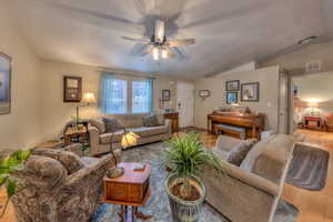 Living room featuring lofted ceiling, light hardwood / wood-style flooring, a textured ceiling, and ceiling fan