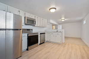 Kitchen featuring sink, white cabinets, stainless steel appliances, and light wood-type flooring