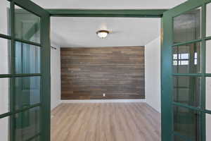 Room featuring light wood-type flooring, a textured ceiling, and wooden walls