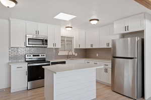 Kitchen with white cabinets, backsplash, a kitchen island, light hardwood / wood-style floors, and stainless steel appliances