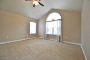 Primary bedroom featuring lofted ceiling, light colored carpet, and ceiling fan