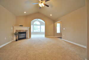 Living room featuring vaulted ceiling, a tiled fireplace, light colored carpet, and ceiling fan