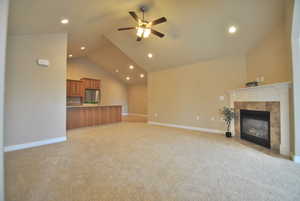 Great room with lofted ceiling, light colored carpet, a gas fireplace, and ceiling fan