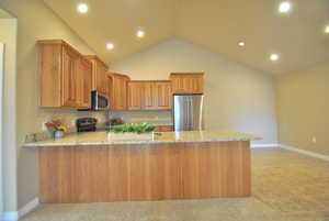 Kitchen featuring light carpet, kitchen peninsula, light stone counters, vaulted ceiling, and stainless steel appliances