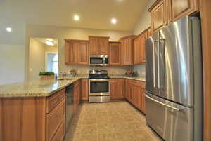 Kitchen featuring lofted ceiling, kitchen peninsula, sink, appliances with stainless steel finishes, and light stone counters