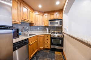 Kitchen featuring sink, decorative backsplash, light stone countertops, and stainless steel appliances