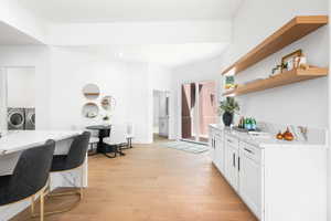 Kitchen featuring light hardwood / wood-style flooring, white cabinets, light stone counters, and washing machine and dryer