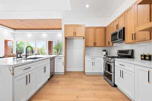 Kitchen with appliances with stainless steel finishes, sink, light wood-type flooring, and white cabinets