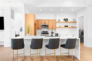 Kitchen featuring tasteful backsplash, appliances with stainless steel finishes, light wood-type flooring, sink, and light stone counters