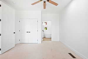 Unfurnished bedroom featuring a closet, light carpet, ensuite bathroom, and ceiling fan