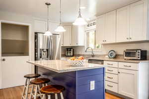 Kitchen featuring a kitchen island, light hardwood / wood-style flooring, light stone countertops, white cabinetry, and appliances with stainless steel finishes