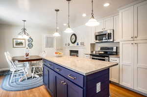 Kitchen with white cabinets, hanging light fixtures, stainless steel appliances, and light wood-type flooring