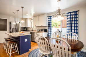 Kitchen with appliances with stainless steel finishes, light hardwood / wood-style flooring, white cabinetry, and a kitchen island