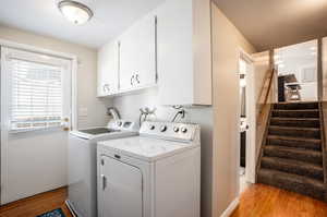 Clothes washing area with cabinets, light hardwood / wood-style flooring, and washing machine and clothes dryer