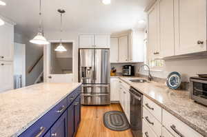 Kitchen with white cabinets, appliances with stainless steel finishes, light hardwood / wood-style flooring, sink, and blue cabinets