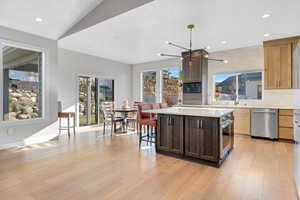 Kitchen featuring appliances with stainless steel finishes, light hardwood / wood-style flooring, a notable chandelier, a kitchen island, and a breakfast bar area