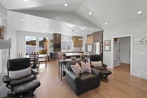 Living room with light hardwood / wood-style floors, vaulted ceiling, and an inviting chandelier