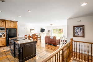 Kitchen with a kitchen island, black appliances, light stone counters, and light hardwood / wood-style floors