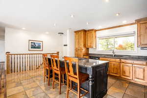 Kitchen with dishwasher, dark stone countertops, sink, a center island, and a kitchen bar