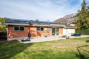 Rear view of property with a mountain view, a patio area, solar panels, and a lawn