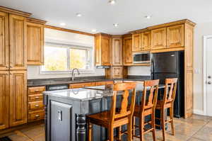 Kitchen featuring black appliances, sink, a kitchen island, ornamental molding, and a breakfast bar area