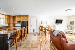 Kitchen featuring light hardwood / wood-style flooring, stainless steel microwave, black fridge, dark stone countertops, and a breakfast bar