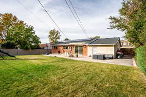 Back of property featuring a patio, solar panels, outdoor lounge area, and a lawn