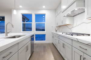 Kitchen with appliances with stainless steel finishes, pendant lighting, white cabinets, dark wood-type flooring, and premium range hood