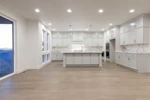 Kitchen featuring light hardwood / wood-style flooring, white cabinetry, a kitchen island with sink, and decorative light fixtures